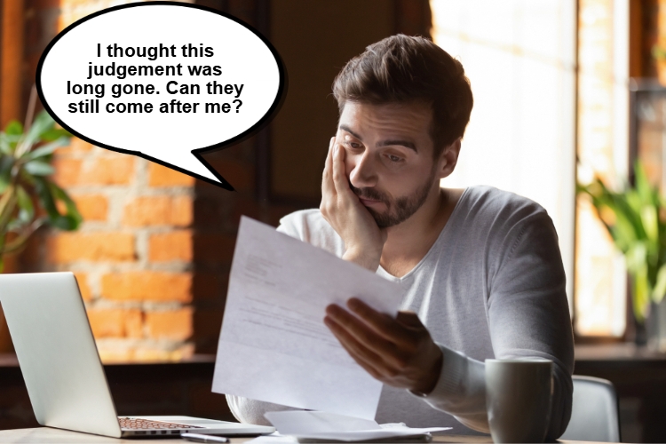 A man sits at a desk with a laptop, looking concerned while reading a document. 