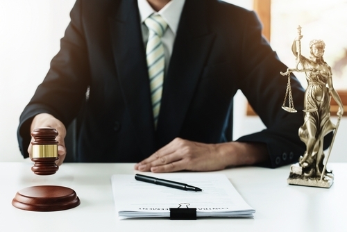 A person in a suit holds a gavel near a clipboard with a pen, contemplating whether a collection agency can sue after 7 years. Nearby, Lady Justice stands as a statuette on the desk.