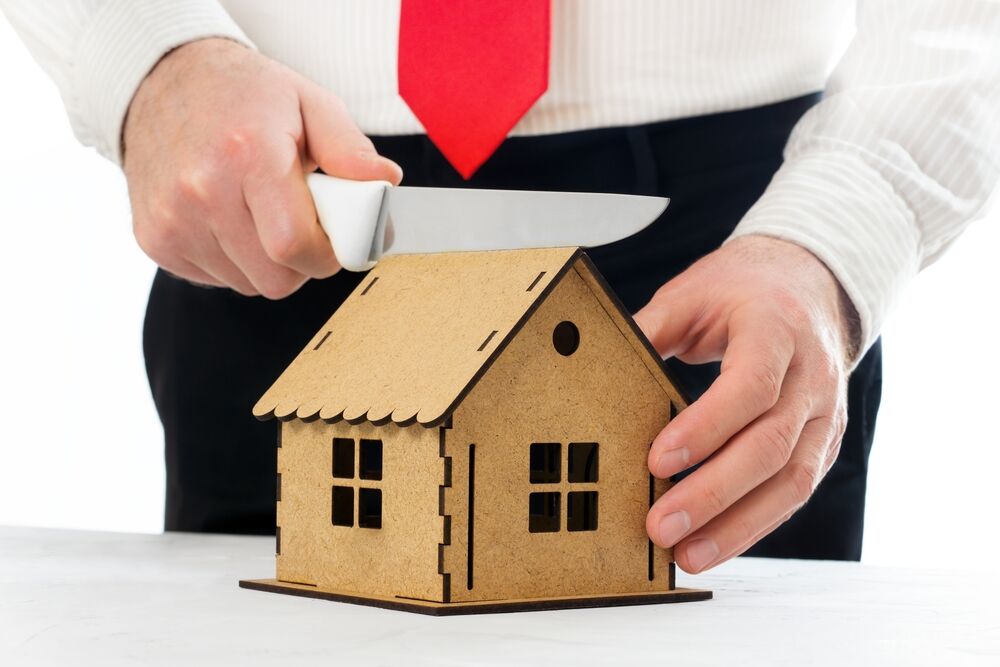 Man cutting a miniature house model with a knife. Assets division in a divorce.