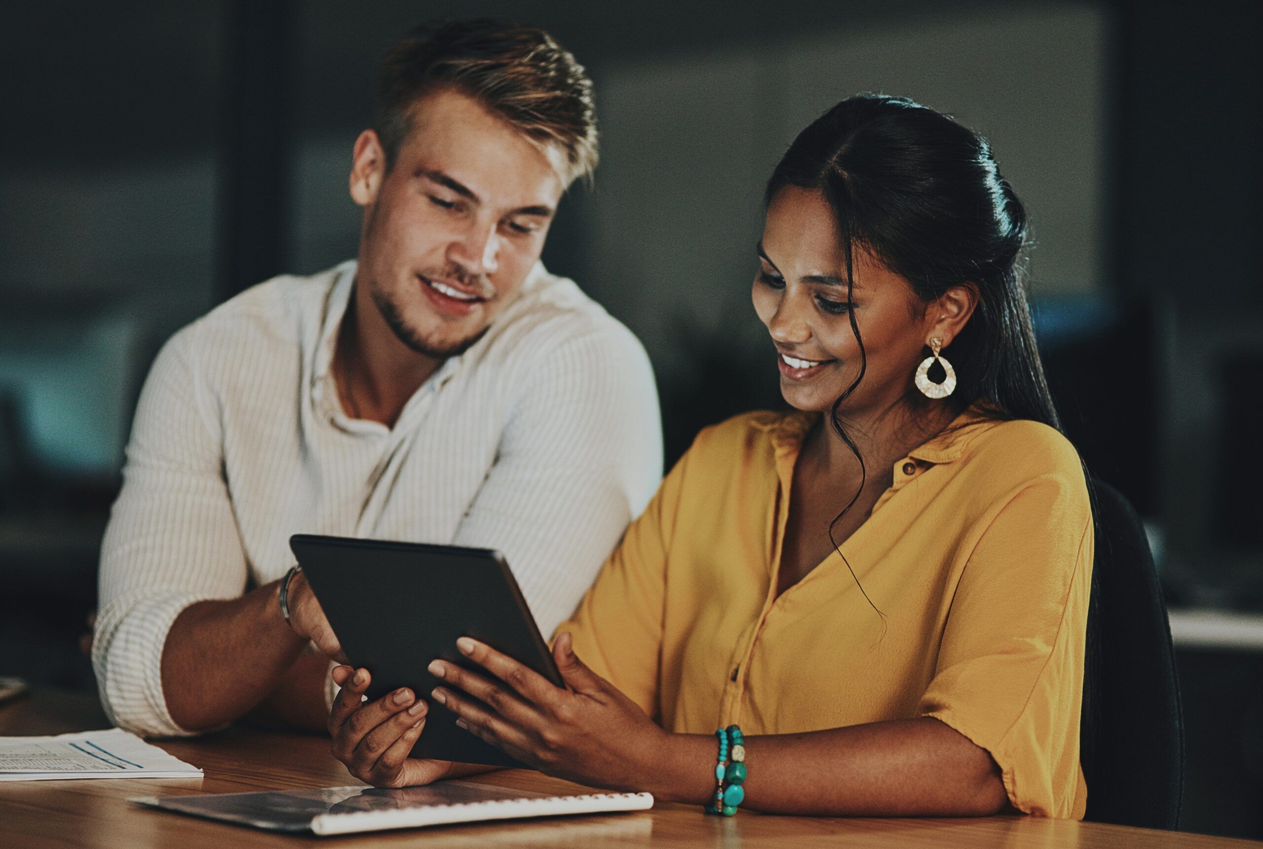 Woman and man sitting at a desk looking at a tablet and smiling
