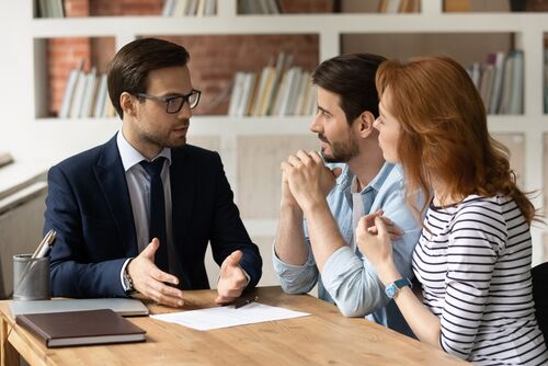 Professional male lawyer financial advisor consulting happy family couple clients in modern office. Interested young customers meeting realtor broker bank worker, discussing agreement or deal.