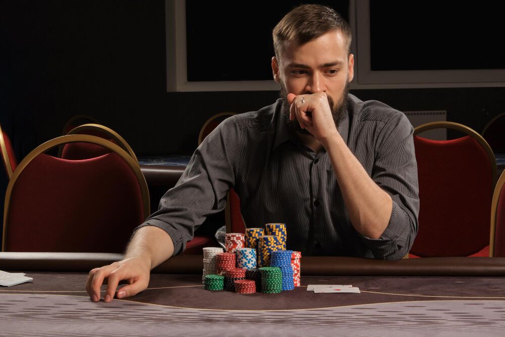 A man sits at a poker table with stacked chips and playing cards in front of him, appearing deep in thought—perhaps considering discharging gambling debt in bankruptcy in Texas.