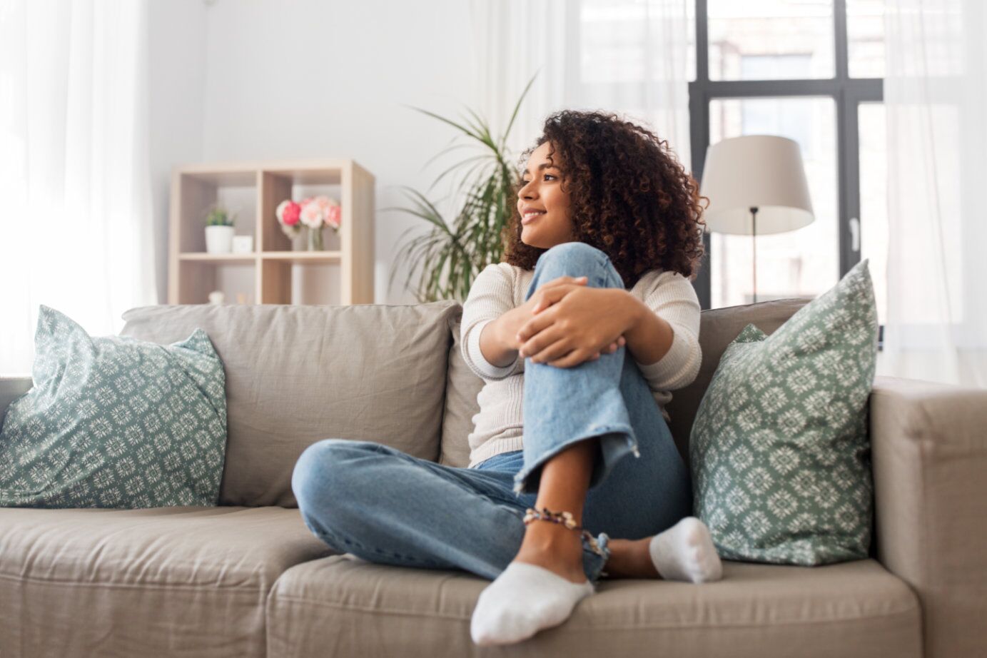 Woman sitting on couch smiling with her arms around her knee