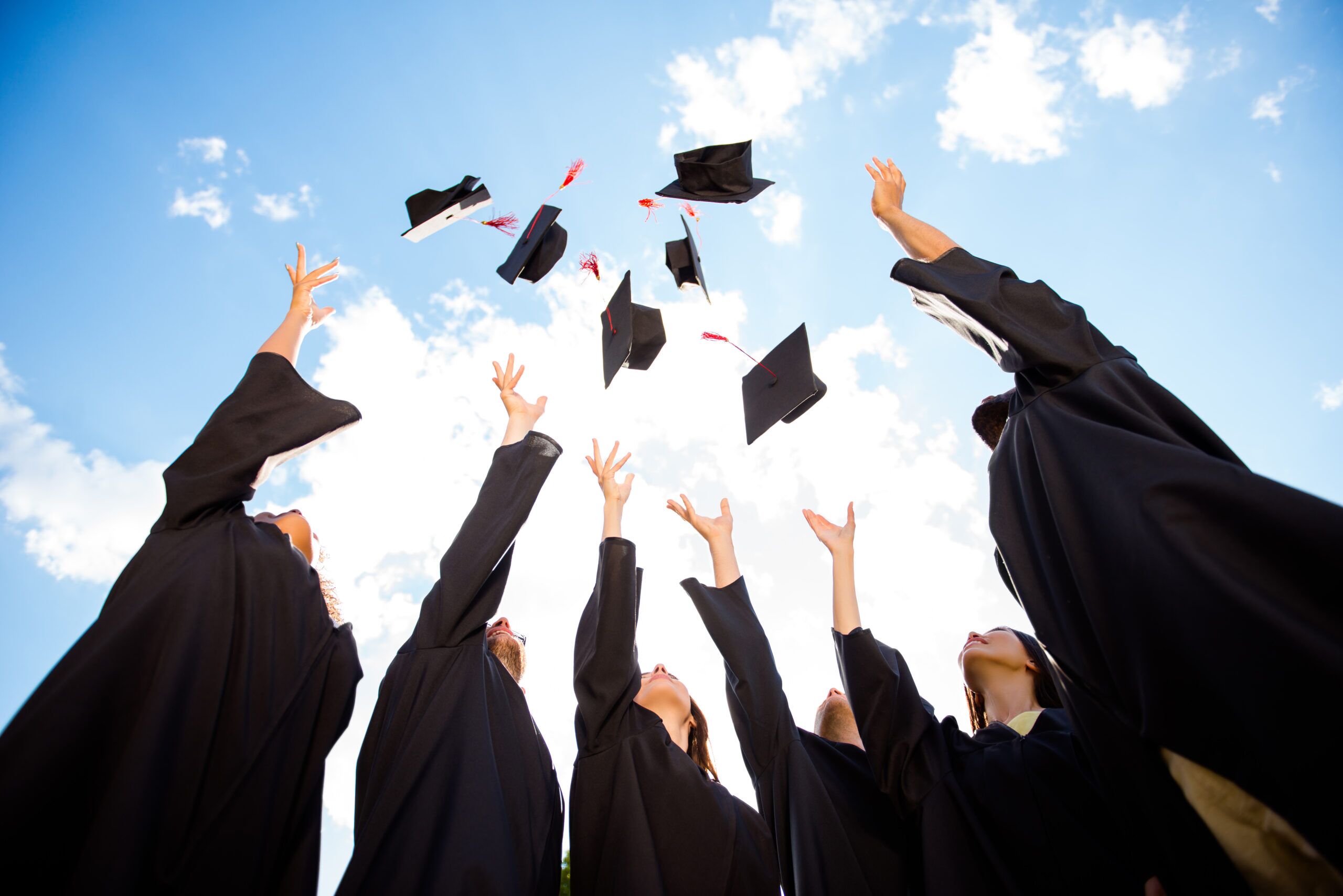 Low angle view of six graduates throwing their caps in the air