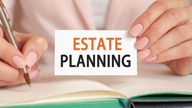 Businesswoman writes in a notebook with a silver pen and hand hold card with text: ESTATE PLANNING
