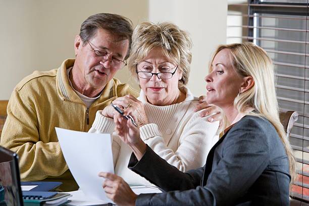 Senior couple talking with financial planner or consultant Senior couple talking with financial planner, consultant or insurance agent, getting advice.  Main focus on older woman in middle. will signing brown 