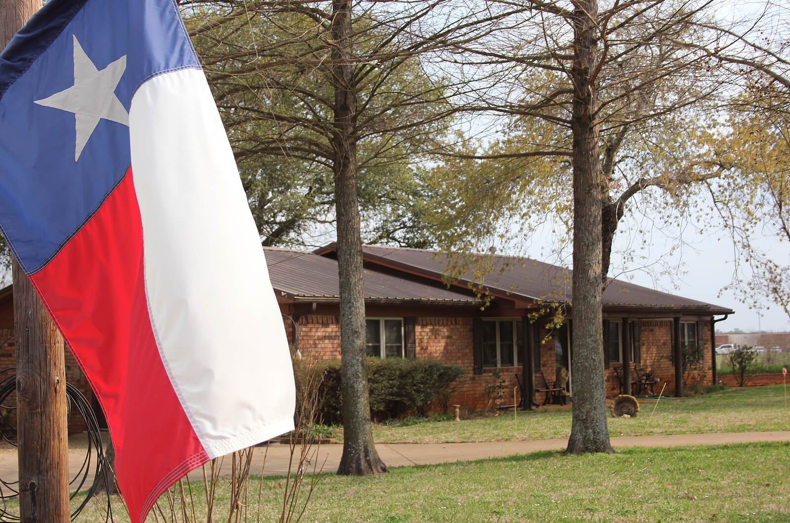 Home with a Texas flag Texas flag with a single story brick home in the background