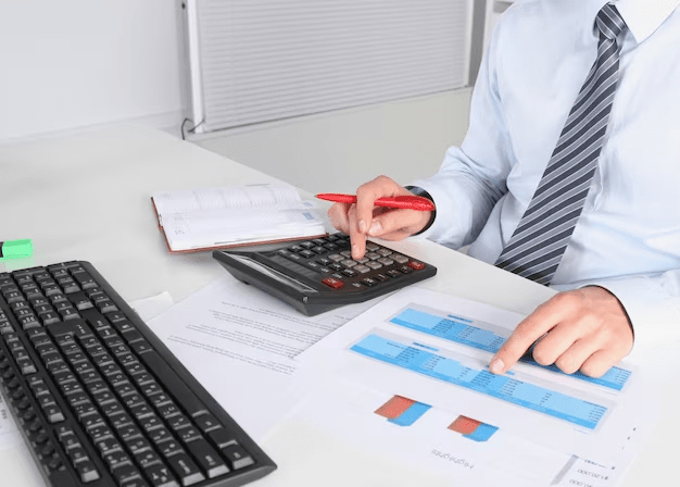 A man in a business suit is using a calculator at his desk while considering how to file Chapter 7 Bankruptcy in Texas.