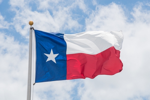 Large Texas (The Lone Star) flag waving on flag pole with cloud blue sky. Windy and sunny day with waving flag blowing/flowing. Ruffled Texas flag. Room for text, copy space.