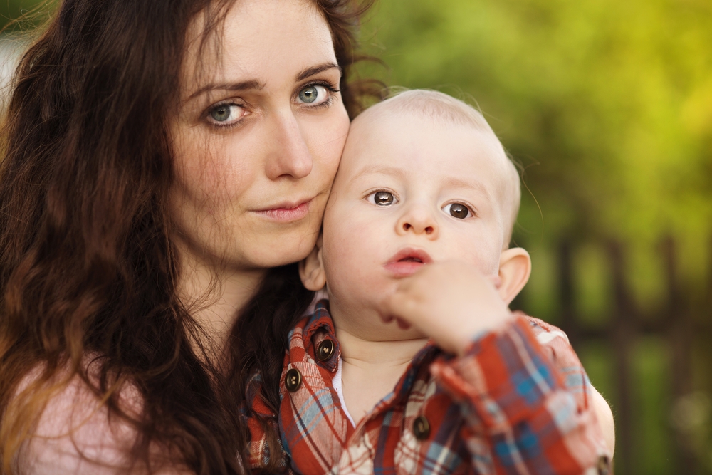 Portrait of a crying little boy who is being held by her mother, outdoors