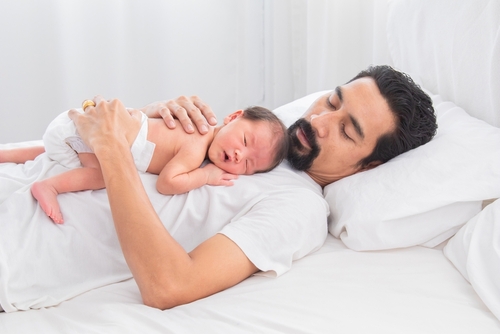 Selective focus of Asian newborn baby sleeping on his father's chest. Dad and son spend time together at home, young dad with cute little infant in his arms. Father and toddler in bed in the morning