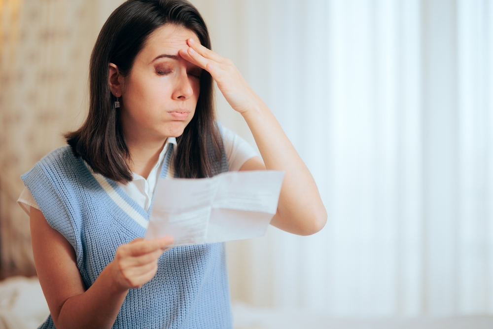 Woman Receiving an Expensive Utility Bill Having a Migraine. Shocked woman receiving the invoice for home electricity service