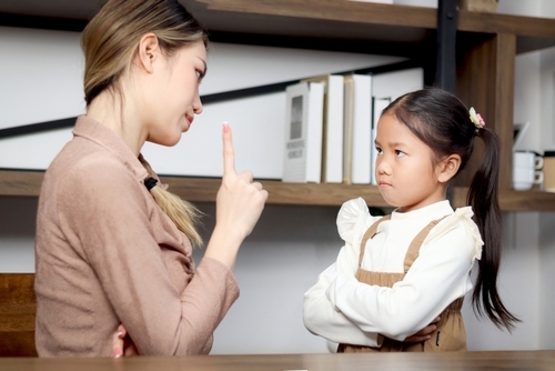 An adult woman gestures with her finger, advising a young girl with crossed arms in an indoor setting, perhaps touching on topics like what you should not do during a custody battle.