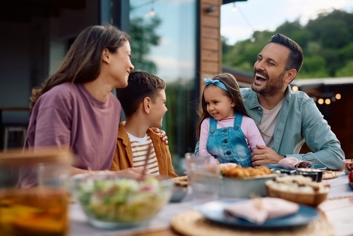 A family of four sits at an outdoor table, smiling and enjoying a meal together—a reminder of the simple joys that should never be overshadowed, even during challenging times like a custody battle.