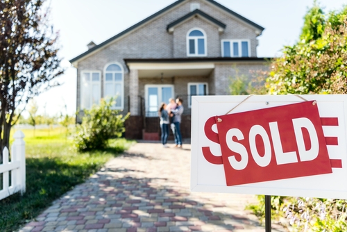 A "Sold" sign is displayed in front of a charming brick house, with a couple standing on the porch, signaling the end of their journey together as they finalize the sale due to divorce.