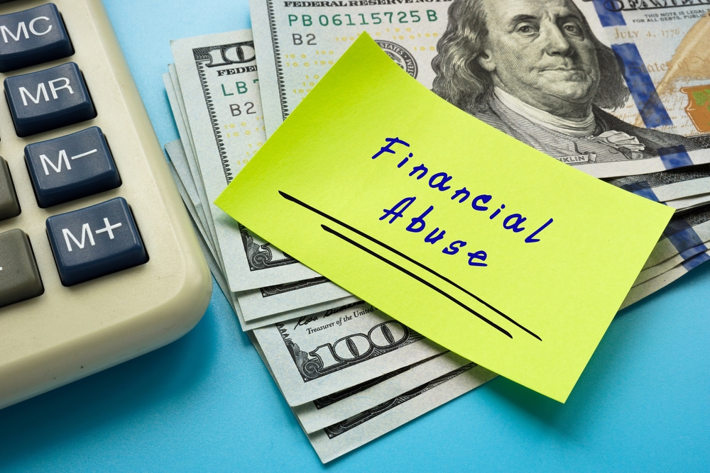 A sticky note labeled "Financial Abuse" placed on a stack of US hundred-dollar bills next to a calculator, highlighting concerns about marital waste during divorce or the impact on a fair divorce settlement.