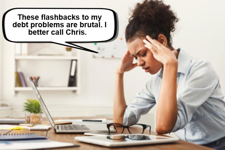 A woman sits at a desk with her head in her hands, looking stressed. 