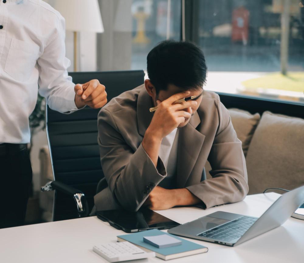 Man at desk looking at computer with his hand over his face