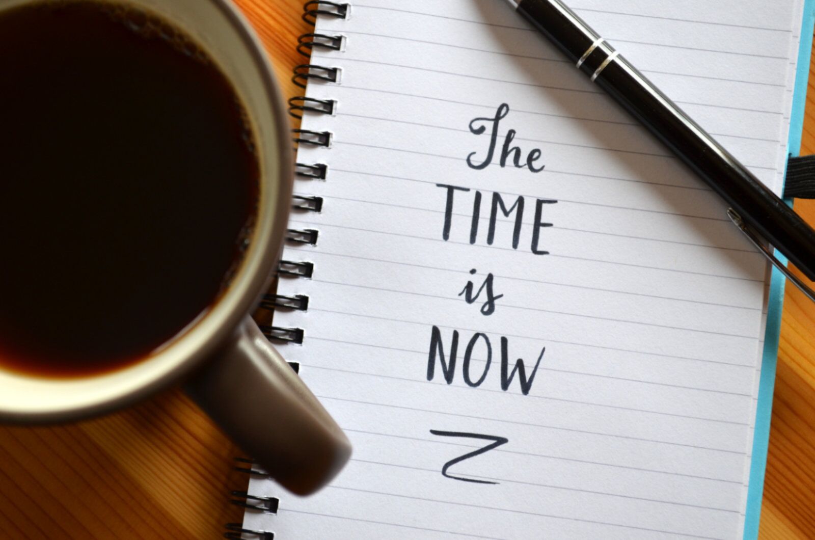 Notebook that says, "The TIME is NOW" with a cup of coffee next to it