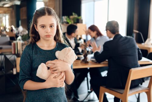Girl hugging teddy bear at law office while parents are in the background with attorney arguing