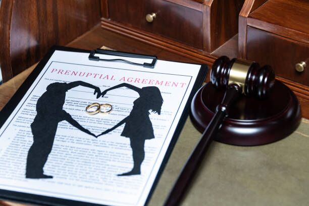 Clipboard holding a prenuptial agreement with a cut-out silhouette of a couple and wedding rings, next to a judge's gavel