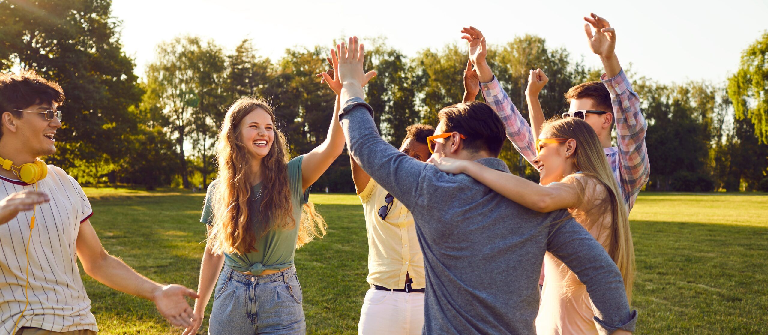 Group of six young friends in a park hugging and high fiving