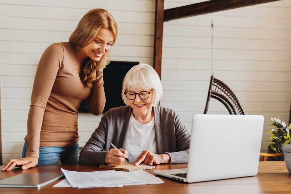 Beauty middle aged lady teaching her mom to use computer, pay domestic bills together online, filling in health insurance, loan, receiving pension on bank account