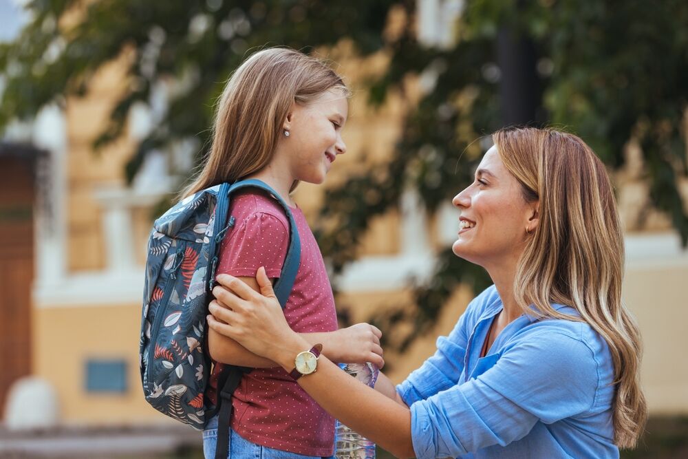 Mother accompanies the child to school. Mom supports and motivates the student. caring mother gently kisses her daughter on the forehead.