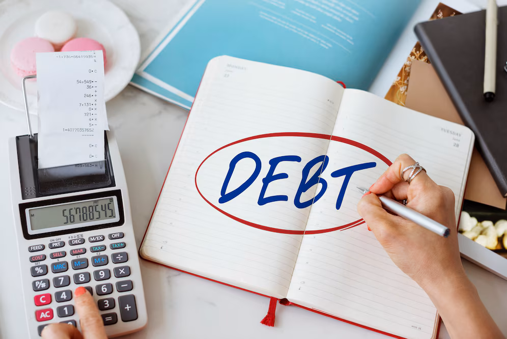 Woman adding up debt on a calculator next to a notebook with the word "DEBT" circled in red