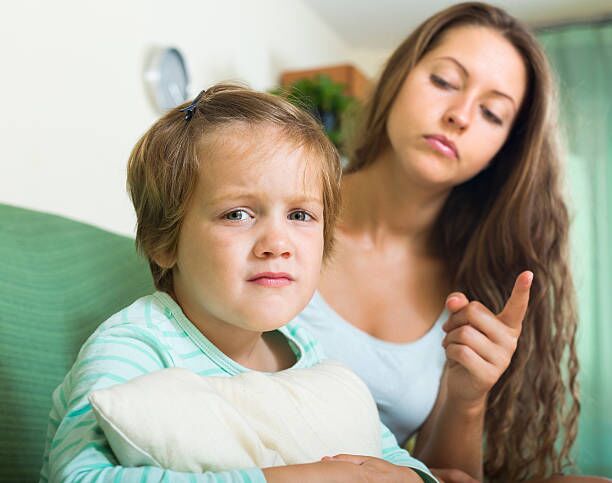 Young mother scolding child who is holding a pillow and staring at camera
