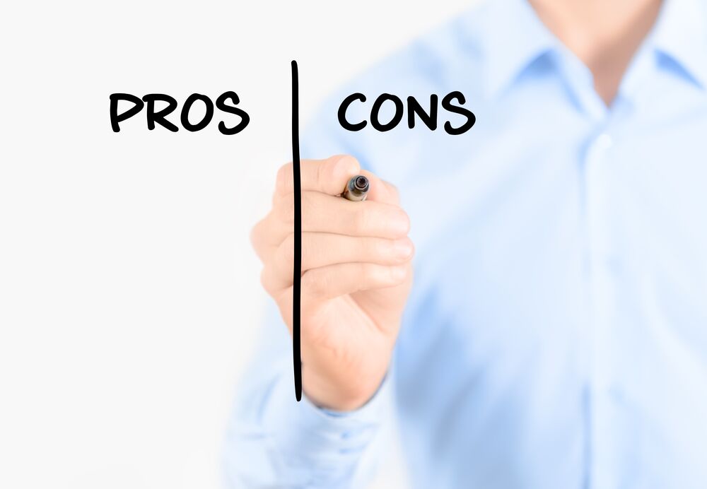 Man in a blue shirt writing "PROS" and "CONS" divided by a vertical line on a clear surface with a marker, as he prepares to weigh his options for Chapter 7.