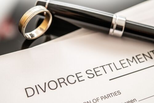 Divorce settlement agreement paperwork displayed alongside a wedding ring and a fountain pen, representing legal processes in family law and the dissolution of marriage.