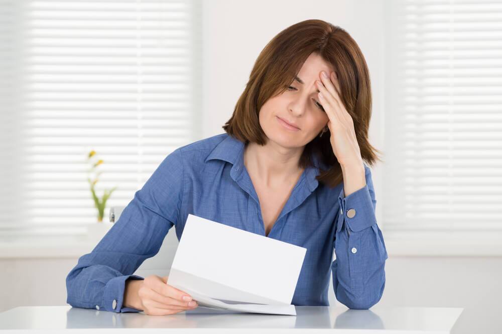 A women looking at a piece of paper with one hand holding the paper and the other on her forehead