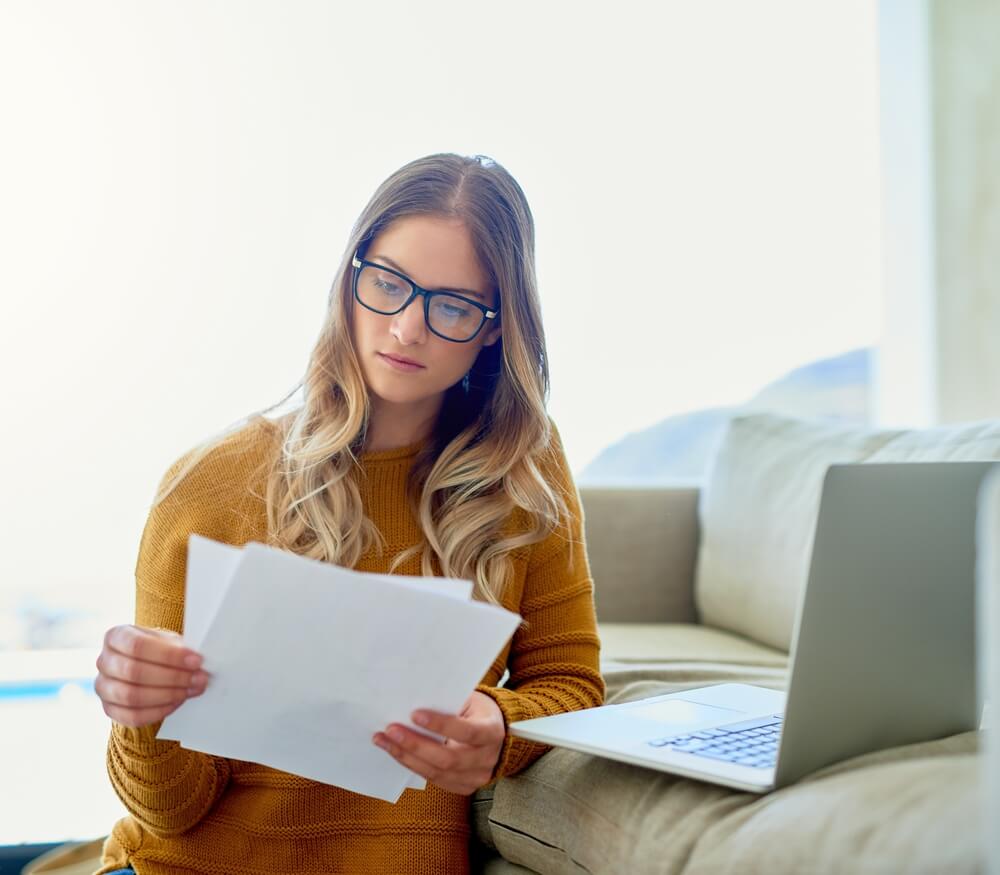 Women sitting down looking over the papers in her hand and her computer is open sitting next to her