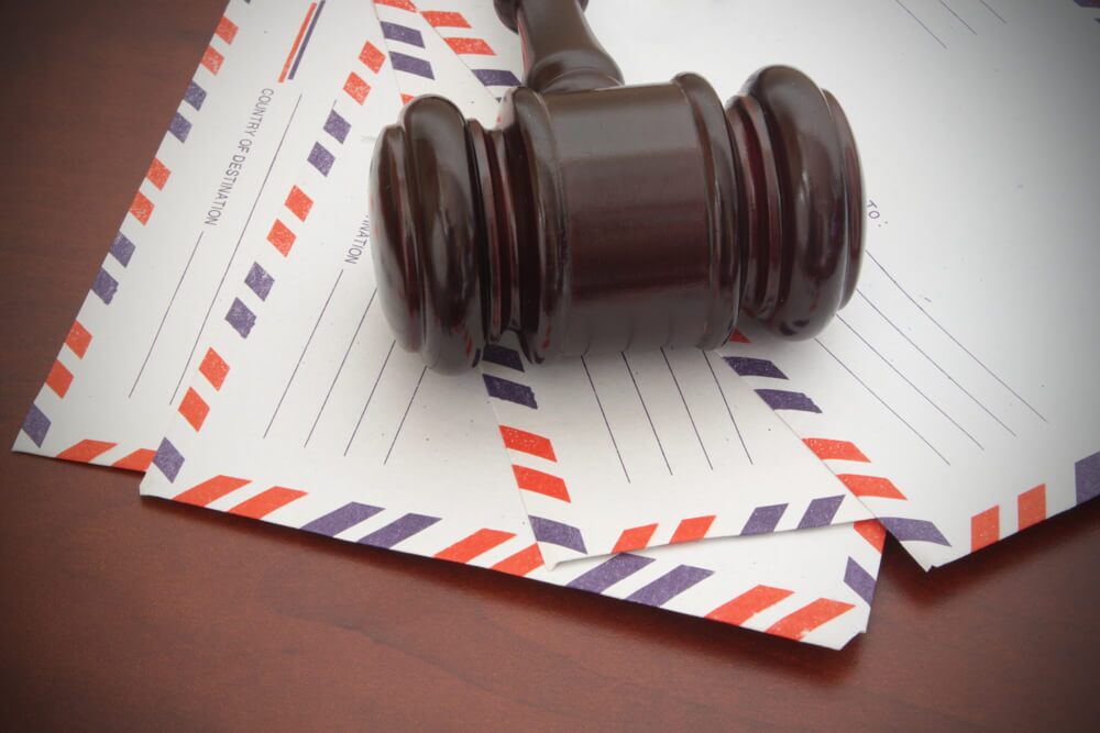 Four mailing envelopes sitting on a wooden table with a judges gavel laying on top of them 