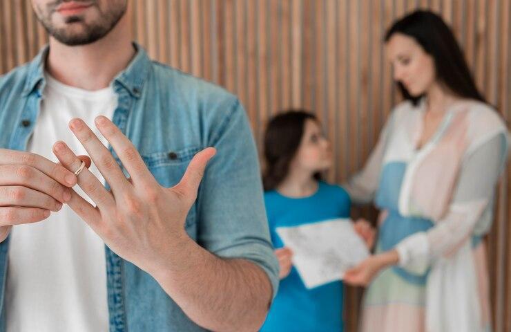 Man removing wedding ring after temporary custody decision, with a woman and child in the background, looking distressed.