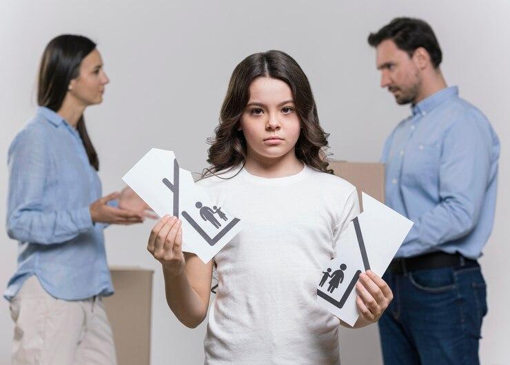 Young girl holding divorce papers, looking sad, with arguing parents in the background discussing temporary custody.